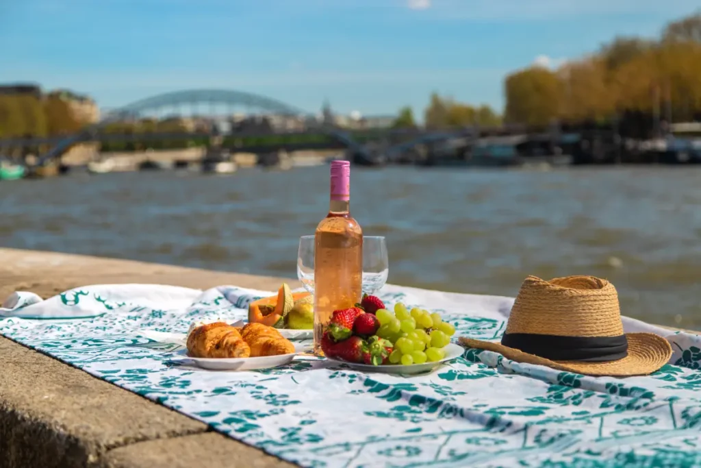 Picnic junto al Sena en París Picnic con vino y fruta junto al río Sena con un puente de París al fondo